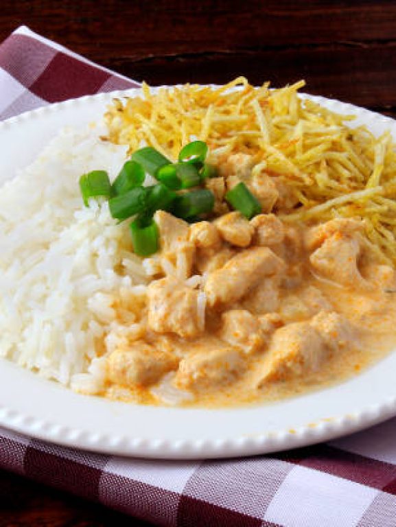 Chicken stroganoff, is a dish originating from Russian cuisine that in Brazil is composed of sour cream with tomato extract, rice and potato chips, on rustic wooden table.